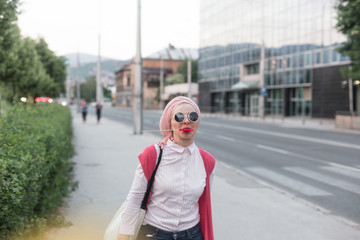 Fototapeta premium romantic portrait of young European Muslim woman with hijab have fun at beautiful sunny day. Image of pretty woman walking with red heart shaped lollipop. She is happy and relaxed.