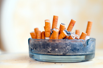 Many cigarette stubs and ash in a glass ashtray on a table