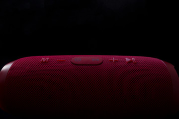 Wireless music speaker. Red bluetooth speaker on black background. Control and volume buttons.