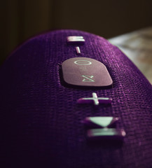 Wireless music speaker. Purple Bluetooth speaker is on the table. Control and volume buttons.