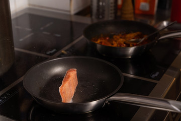 Chief is frying a piece of raw salmon on a pan in  a restaurant kitchen