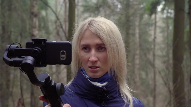 Young girl blogger makes video with her phone and gimbal in the forest on the nature.