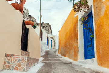 Fototapeta na wymiar Old street in Akrotiri village on Santorini island, Greece. View of castle and blue doors. Traditional architecture.