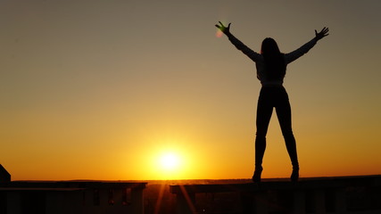 Fototapeta premium Young girl in sports uniform sits on the edge of the roof during sunset.