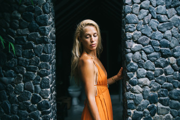 Pensive woman in orange dress standing between stone walls of Balinese building