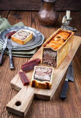 Traditional French Pate en croute with goose meat and liver ofered with quince cheese as closeup on a modern design wooden board