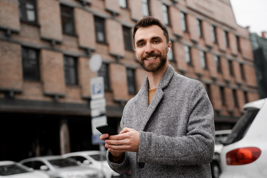 Adult bearded business man walking urban street using mobile cell phone and waiting taxi, searching online taxi service application, modern digital technologies and fast internet. Smiling to camera
