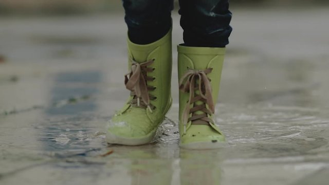 Little boy in rubber boots stands in a puddle during the rain