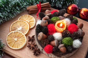 Christmas composition - lit candle wax, cones, acorns, balls, dried orange, anise, cinnamon. On wooden background.