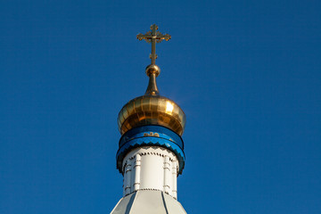 Fototapeta na wymiar The dome of an Orthodox church with a cross on a background of blue sky. Dome and cross of gold color.
