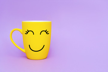 Smiley yellow coffee cup on purple background. Happy friday word concept. Minimalism style, romantic mood, good morning, happiness, break time