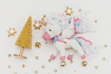 knitted flying unicorn on a white background with a Christmas tree and golden stars