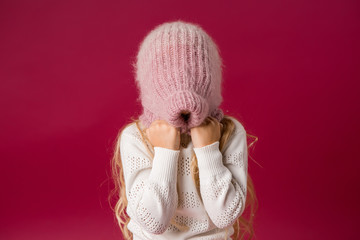 little blonde girl in a knitted hat and sweater catches the snow and laughs. winter clothes. isolate on red background, space for text