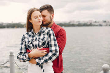 Cute couple in a park near river. Lady in a chirt. Guy in a red shirt