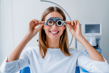 Young woman checking vision with eye test glasses during a medical examination at the ophthalmological office - Powered by Adobe