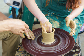 the Hands of a master and a student on a Potters wheel sculpt a pitcher of clay