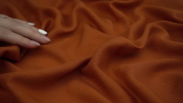 Touching sensitive rust colored fabric in slow motion. Woman's hand softly strokes a textile.