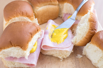 Putting mustard on a ham on roll sandwich.