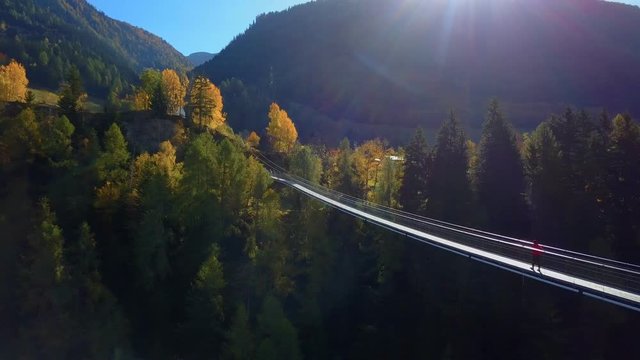 Man walks on hanging rope river bridge in forest