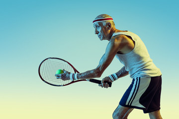 Senior man wearing sportwear playing tennis on gradient background, neon light. Caucasian male model in great shape stays active, sportive. Concept of sport, activity, movement, wellbeing, confidence.