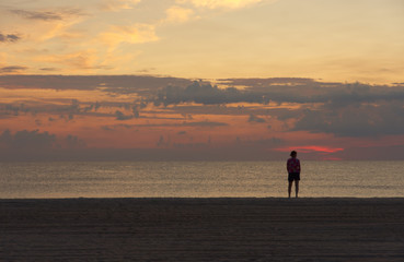 Fototapeta na wymiar dawn at beach woman pondering the surf and pastel colored sky