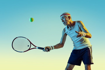 Senior man wearing sportwear playing tennis on gradient background, neon light. Caucasian male model in great shape stays active, sportive. Concept of sport, activity, movement, wellbeing, confidence.