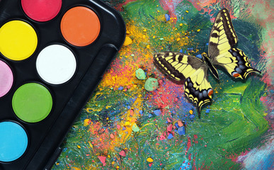 Colorful butterfly and artist paints. art paints. watercolor, pastel crayons and a palette with...