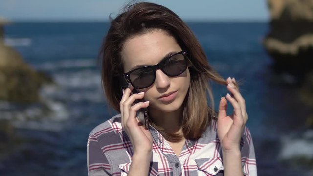 A young woman makes calls on a smartphone on the background of the sea. Woman with a phone on vacation. Blue sea in sunny weather
