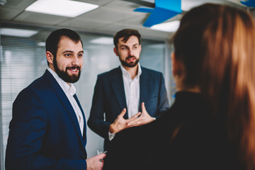 Back view of talented female standing in modern office during formal meeting with experienced male colleagues.Young skilled smart traders analyzing information and discussing creative ideas in office
