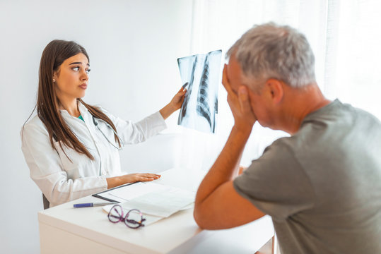 Pneumology Consultation Man. Doctor examining chest x-ray film with patient at hospital. Doctor examining at lungs radiograph x-ray film of patient. Doctor explaining x-ray results to senior patient