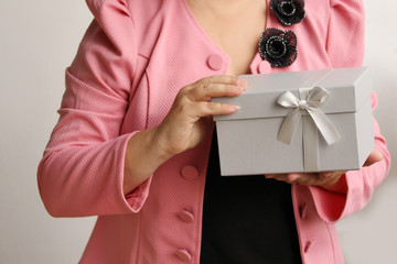 woman holding a gift in a light gray box with a satin ribbon and a bow, concept of Valentine's Day, Christmas presents, mother's day, new year, close-up, copy space
