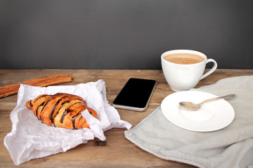 phone and cappuccino coffee in a white cup and saucer and chocolate muffin in paper on an old wooden table, coffee maker, food enjoyment concept