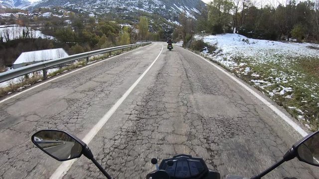 Driving a motorbike in first person on a rural road in winter with snow in the road and the mountains covered with snow in the background.
