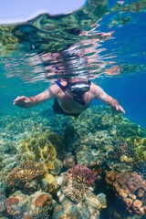 Man snorkeling above tropical coral reef in the transparent water