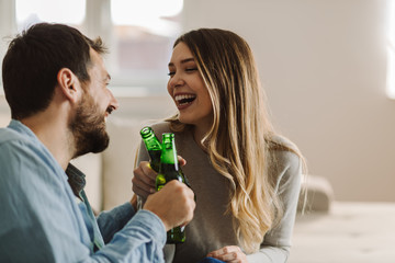 Happy couple toasting with beer whille communicating on sofa in the living room
