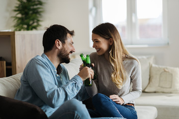Happy couple toasting with beer whille communicating on sofa in the living room