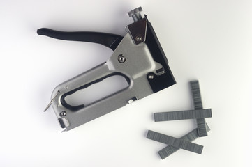  black and silver stapler and four brackets on a white background. Flat lay