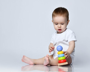Newborn baby boy toddler playing and playing with a childrens multi-colored developing pyramid on a gray