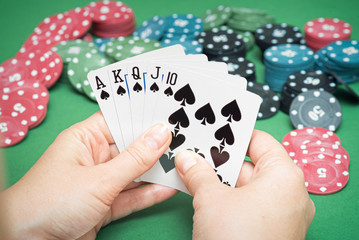 Royal Flush cards in female hands and poker chips on green flat lay background.