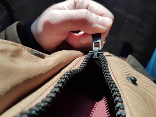 The man's hand zips zip up on the jacket. Zipper close up in hard light. © Northern life
