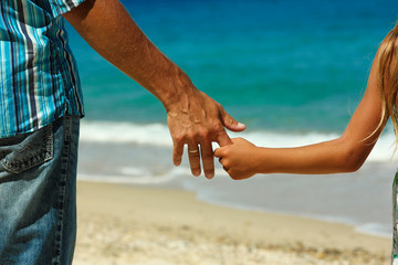 The parent holds the child's hand on the beach