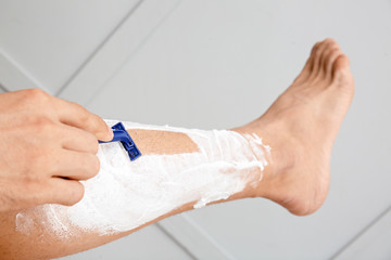 Handsome young man shaving leg on light background