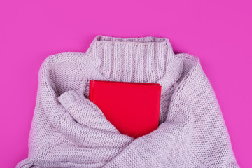 A soft knitted purple sweater with a red notebook on a pink background.