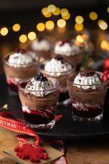 Dessert in a glasses with chocolate and berries spread on wooden background with garland lights bokeh and christmas decoration. New year holidays background concept. Dessert recipe ideas.