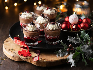 Dessert in a glasses with chocolate and berries spread on wooden background with garland lights bokeh and christmas decoration. New year holidays background concept. Dessert recipe ideas.