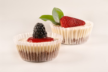 Front view and close-up of two homemade cheesecakes with homemade strawberry sauce and accompanied by strawberries, blackberries, raspberries and green leaves on white background. 
