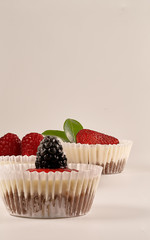 Vertical photo and close-up of  homemade cheesecakes with homemade strawberry sauce and accompanied by strawberries, blackberries, raspberries and green leaves on white background. 