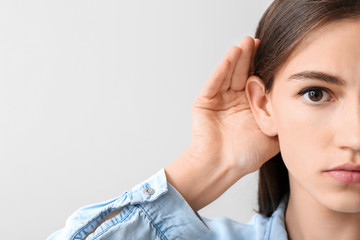 Young woman with hearing problem on light background