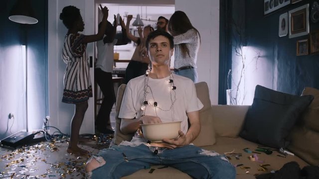 Camera zooms in on young Caucasian man addicted to movies, happy dancing party crowd in the background slow motion.