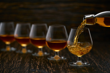 Pouring cognac from the bottle into the glass against wooden background.